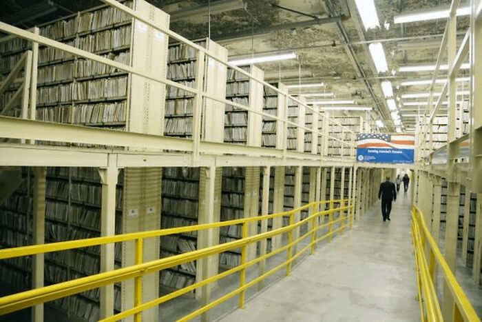 Historical photo of a large archive room with endless shelves filled with documents, showcasing how people organized records decades ago.