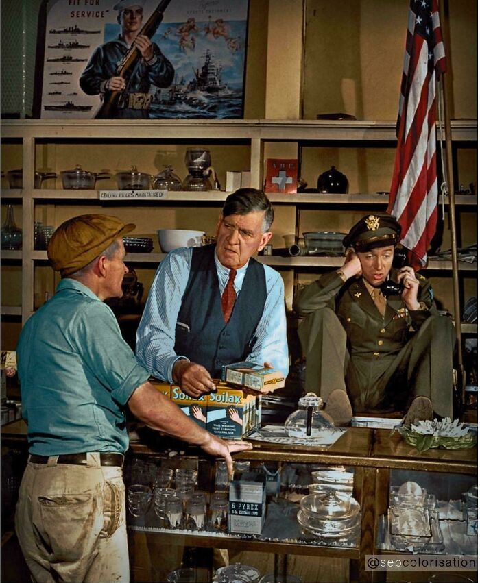 Three men in a historical shop setting, one in military uniform, engaging in conversation with vintage items around.