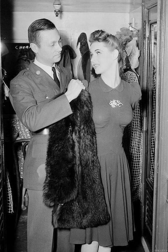 "Historical photo of a man in military uniform and woman in dress, holding a fur coat in a vintage setting."