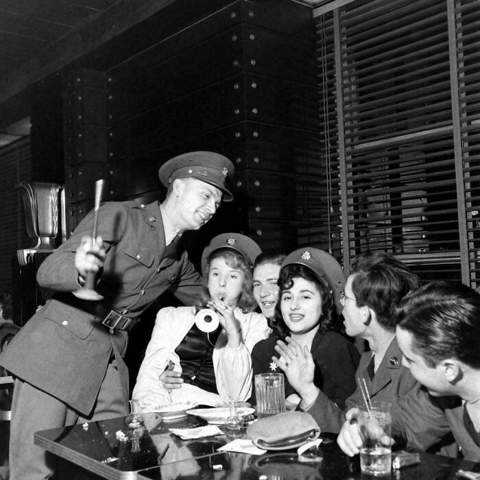 Group of people in military uniforms socializing at a table, capturing historical moments from decades ago.