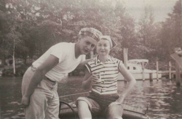 Two people in vintage attire posing by a lake, embodying how people lived decades ago.