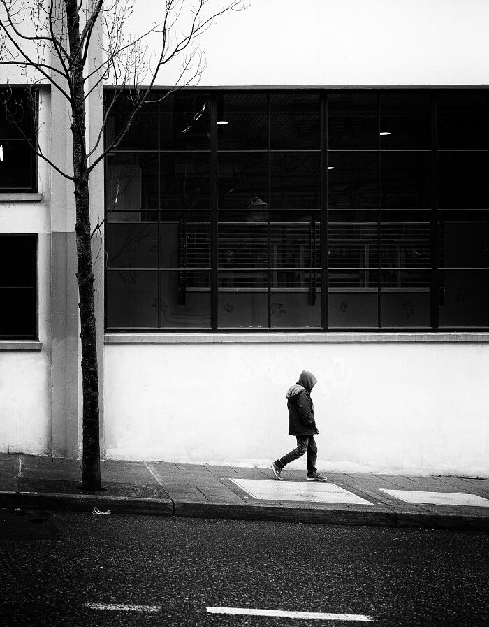 Person in a hooded jacket walking alone on a city sidewalk; evokes eerie unsolved mysteries atmosphere.