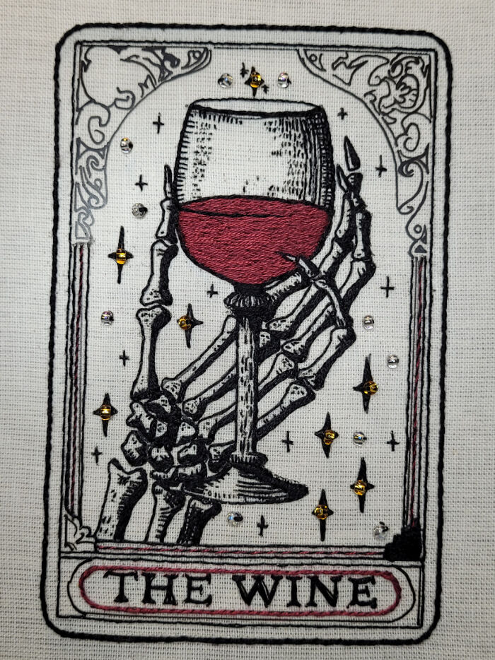 Skeleton hand embroidery holding a wine glass with red wine, detailed stitching and decorative accents showcasing incredible embroidery skills.