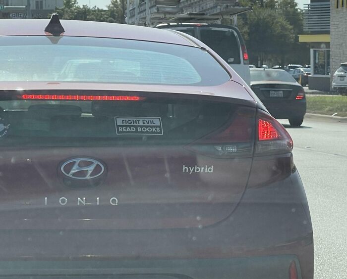 Red Hyundai Ioniq with a funny bumper sticker saying "FIGHT EVIL READ BOOKS" on the back window in traffic.