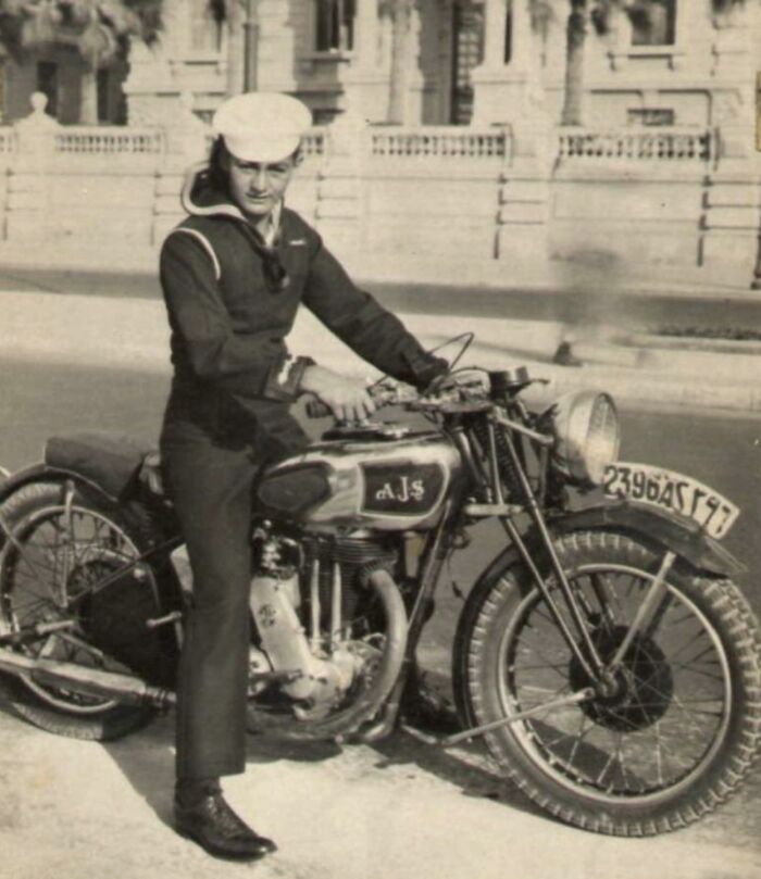 Vintage photo of a sailor in uniform sitting on a classic AJS motorcycle, showcasing historical lifestyles.