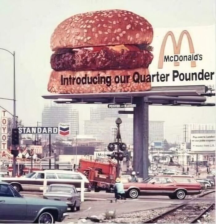 Vintage McDonald's billboard with a large burger and 1960s cars, showcasing historical advertising methods.