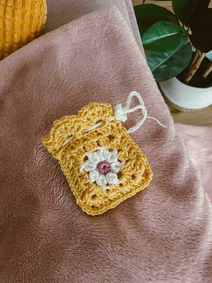 Yellow crochet piece with white flower design resting on a soft pink fabric, showcasing detailed crochet masterpieces.