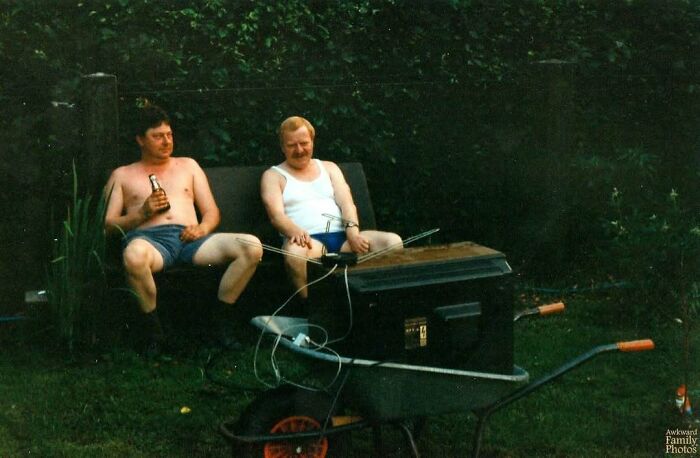 Two men in casual summer clothes sitting awkwardly outside, sharing a relaxed moment in an awkward family photo.