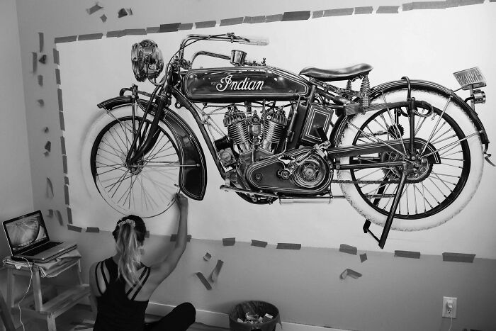 Artist drawing an intricate Indian motorcycle on a wall, capturing fascinating details with black and white tones.