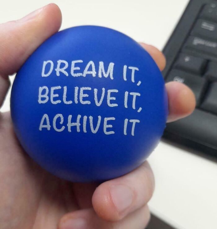 A blue stress ball with a motivational typo slogan held in hand, related to infuriating company gifts bonuses.