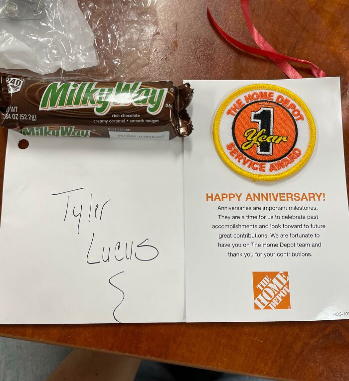 Milky Way bar and 1-year service award patch on a table, representing infuriating company gifts bonuses concept.