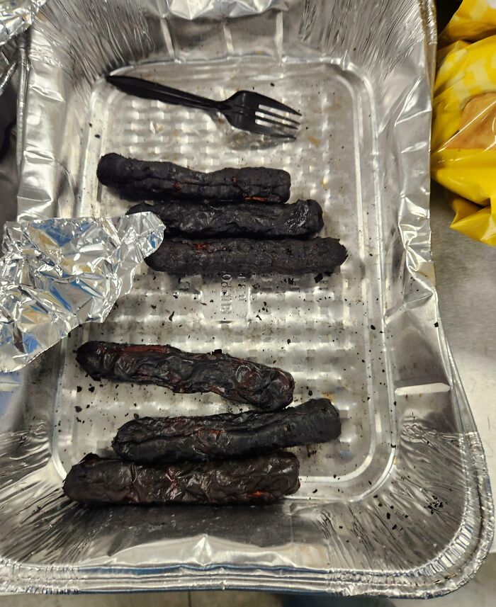 Charred sausages in a foil tray with a plastic fork, illustrating infuriating company gifts bonuses.