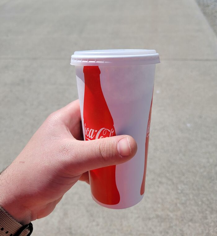 Hand holding a Coca-Cola cup outdoors, symbolizing infuriating company gifts.