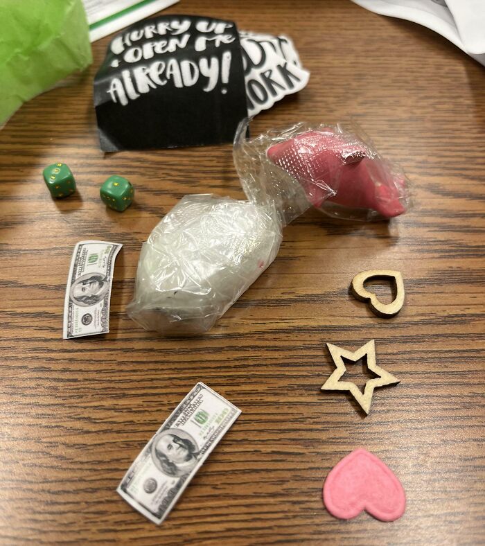 Assorted infuriating company gifts on a wooden table, including dice, fake money, and novelty items.