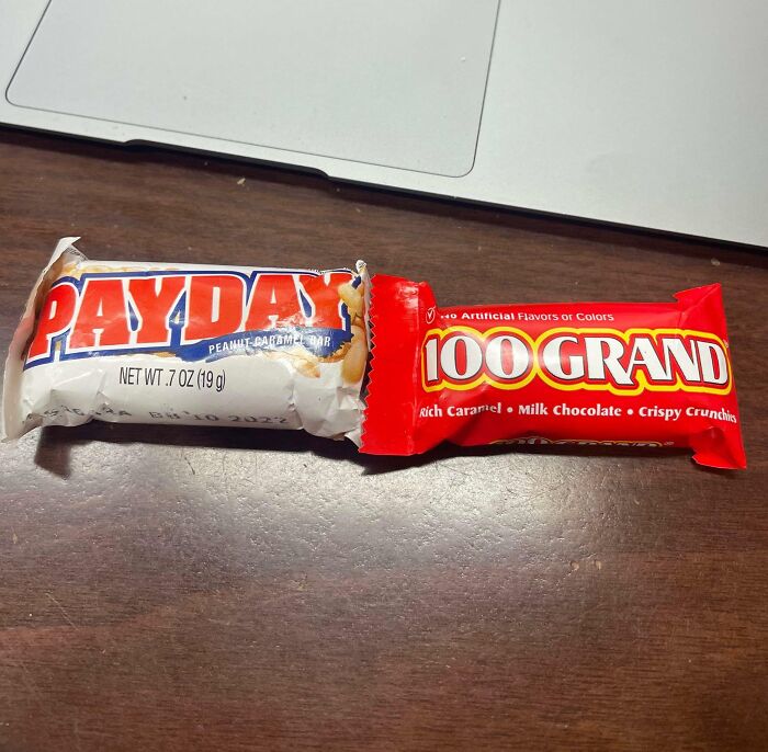 "Infuriating company gifts: Payday and 100 Grand candy bars on a desk near a laptop."