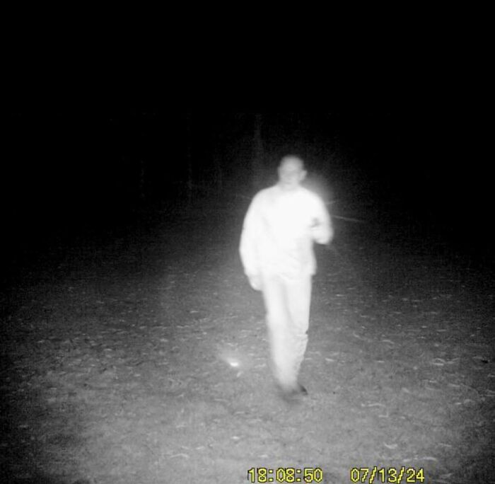 A mysterious figure captured at night on a trail cam, emitting an eerie glow.