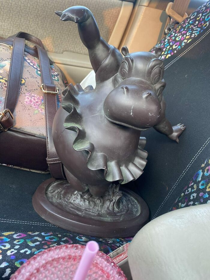Hippo statue in tutu found secondhand, placed on car seat with floral bag.