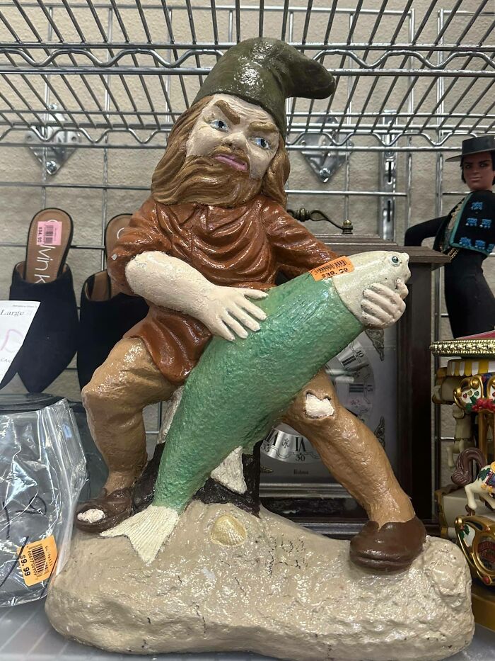 Gnome statue holding a large fish, a quirky secondhand find on display.