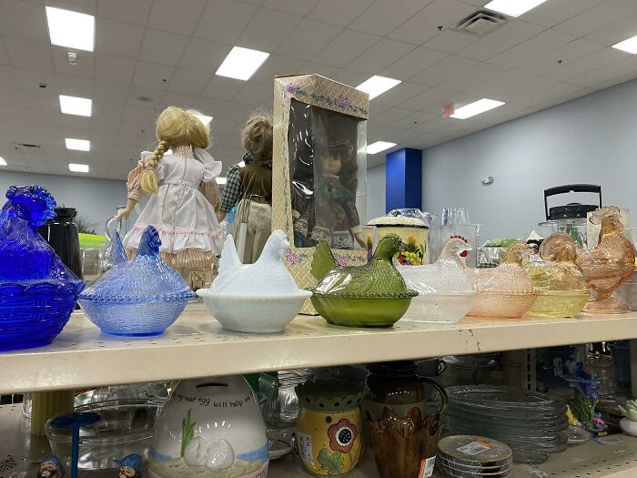 Secondhand finds: colorful glass hen dishes and dolls on a thrift store shelf.