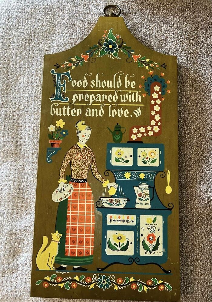 Decorative kitchen sign with a painted woman and cat, with text: "Food should be prepared with butter and love." Secondhand finds.