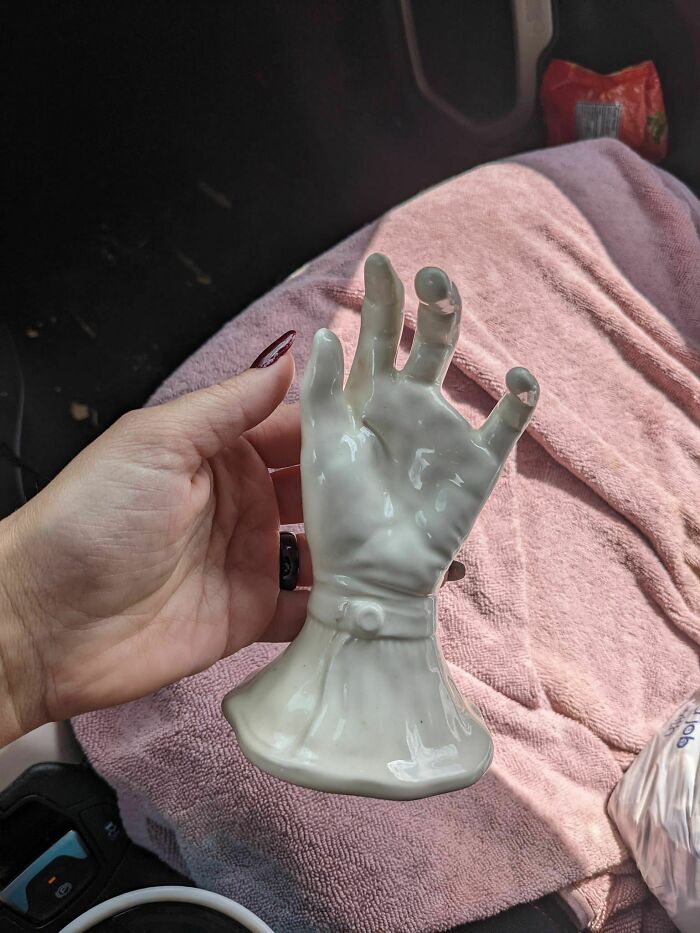 A ceramic hand sculpture as a secondhand find, held up in a car with a pink towel background.
