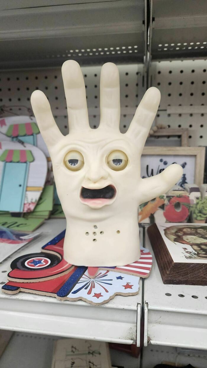 Weird secondhand find of a hand-shaped ornament with a face and open mouth on a store shelf.