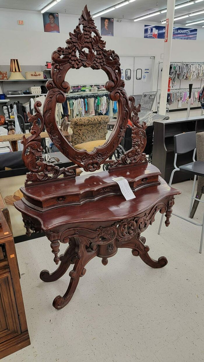 Intricately carved wooden antique vanity with an oval mirror on display in a secondhand store.