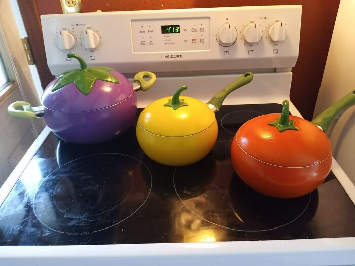 Colorful vegetable-themed pots found in a secondhand store, sitting on a stovetop.