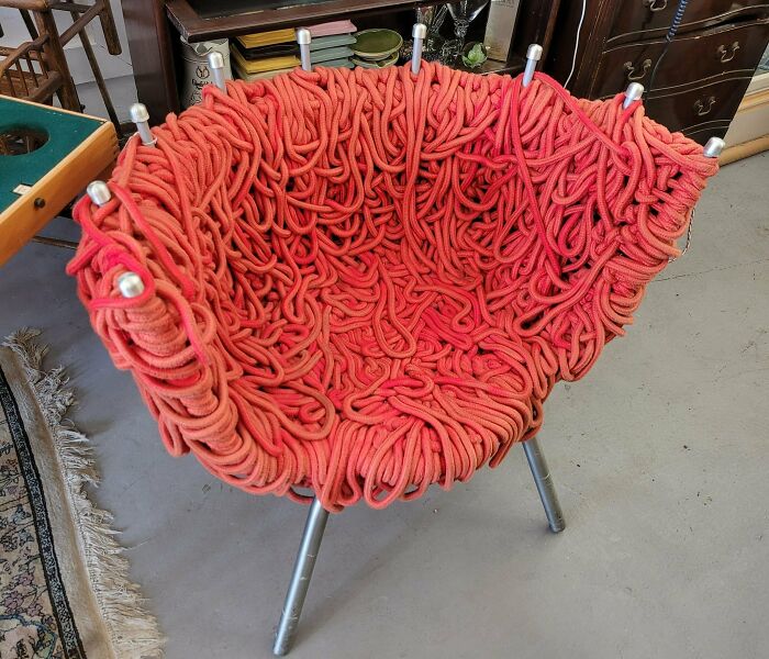 Unique secondhand chair made of red tangled ropes on metal legs.