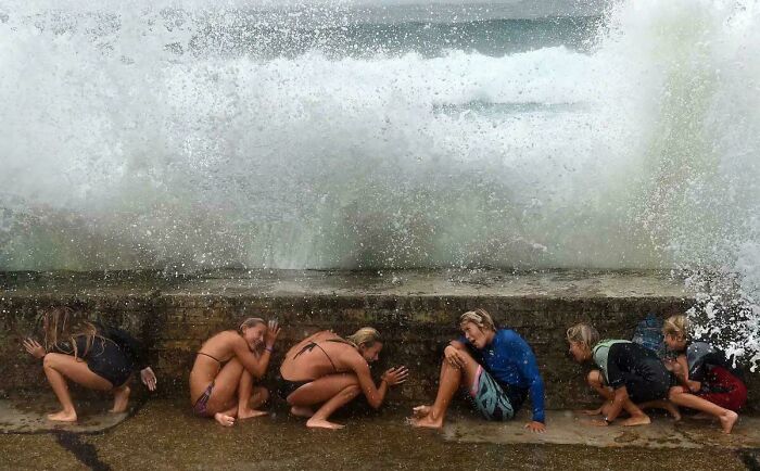 People crouching near a wall as waves crash over, creating an accidental Renaissance-like scene.