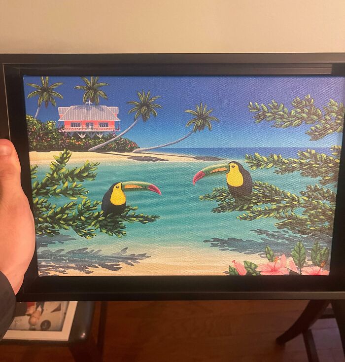 A hand holding a framed painting of a tropical scene with toucans, may represent company gifts.