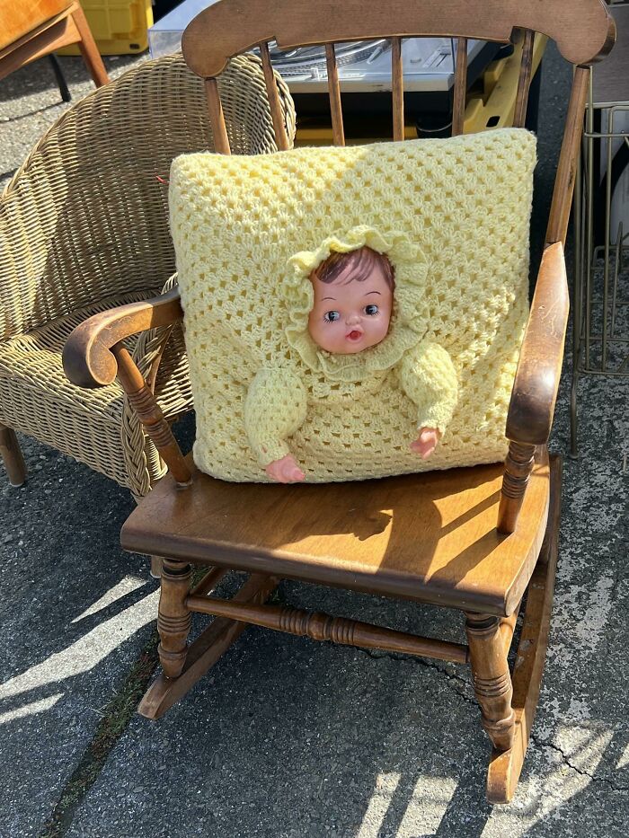 Weird secondhand find: doll head on a crocheted pillow in a wooden rocking chair.
