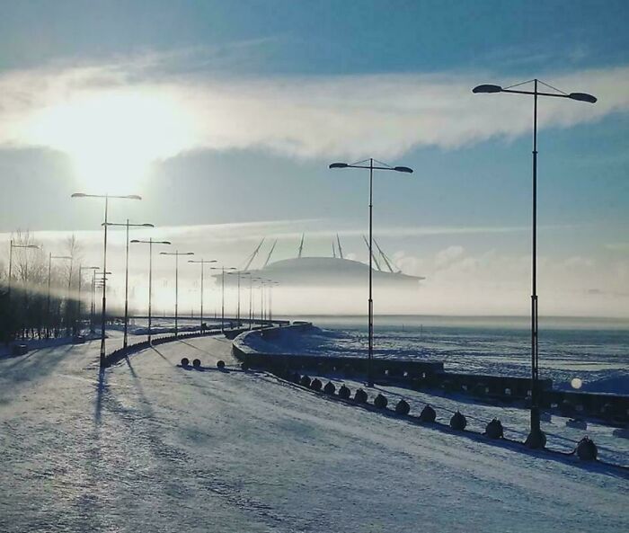 Foggy coastal road with streetlights leading to a massive, mist-shrouded structure illustrating megalophobia concept.