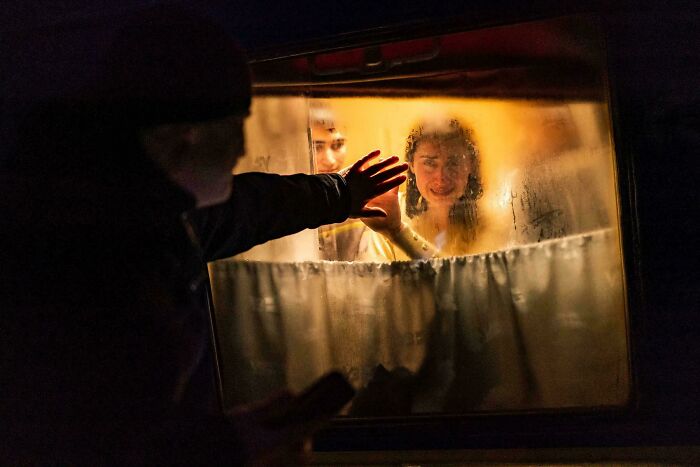 Person reaching towards a window at night, with two people on the other side, creating an accidental Renaissance effect.