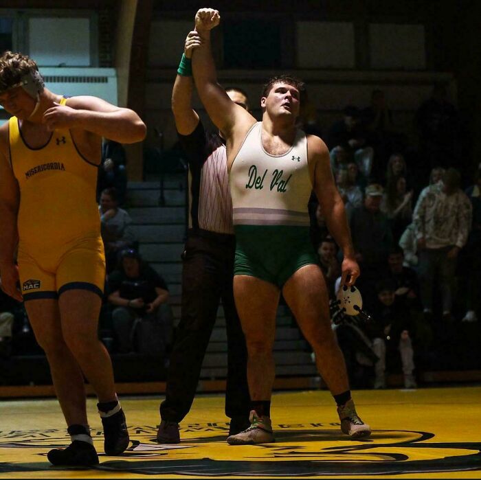 Wrestler's victory pose captures an accidental Renaissance scene on the mat, under dramatic lighting.