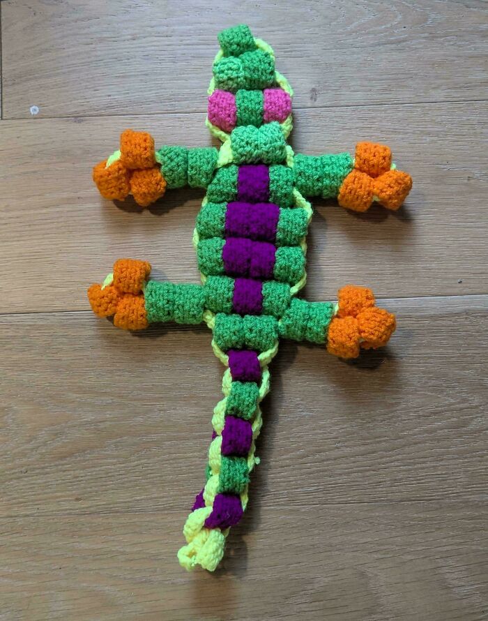 Crochet masterpiece of a colorful lizard with green, purple, orange, and yellow yarn on a wooden surface.