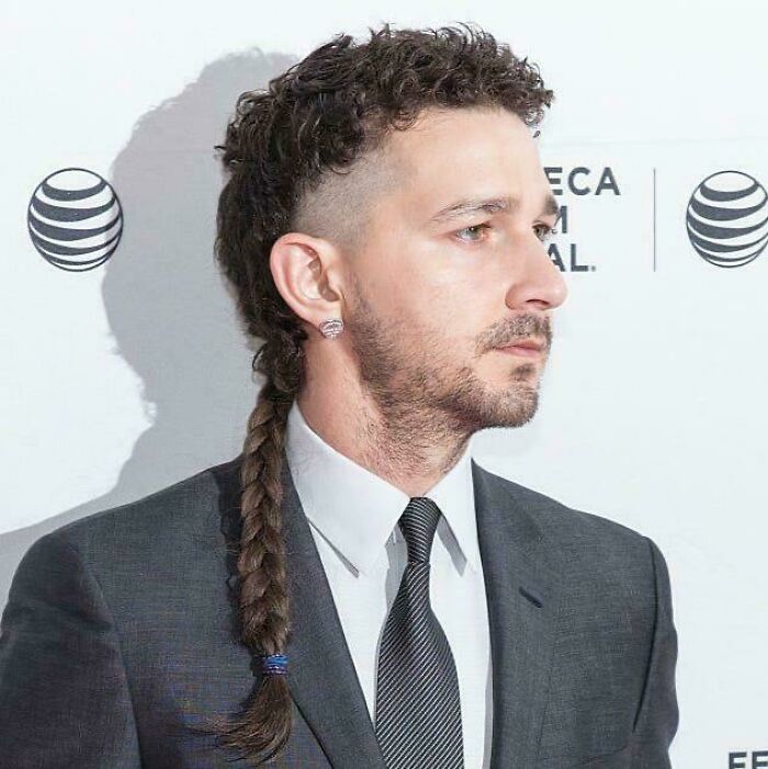 Shia LaBeouf with an unfortunate haircut featuring shaved sides, curly top, and a long braided rat tail.