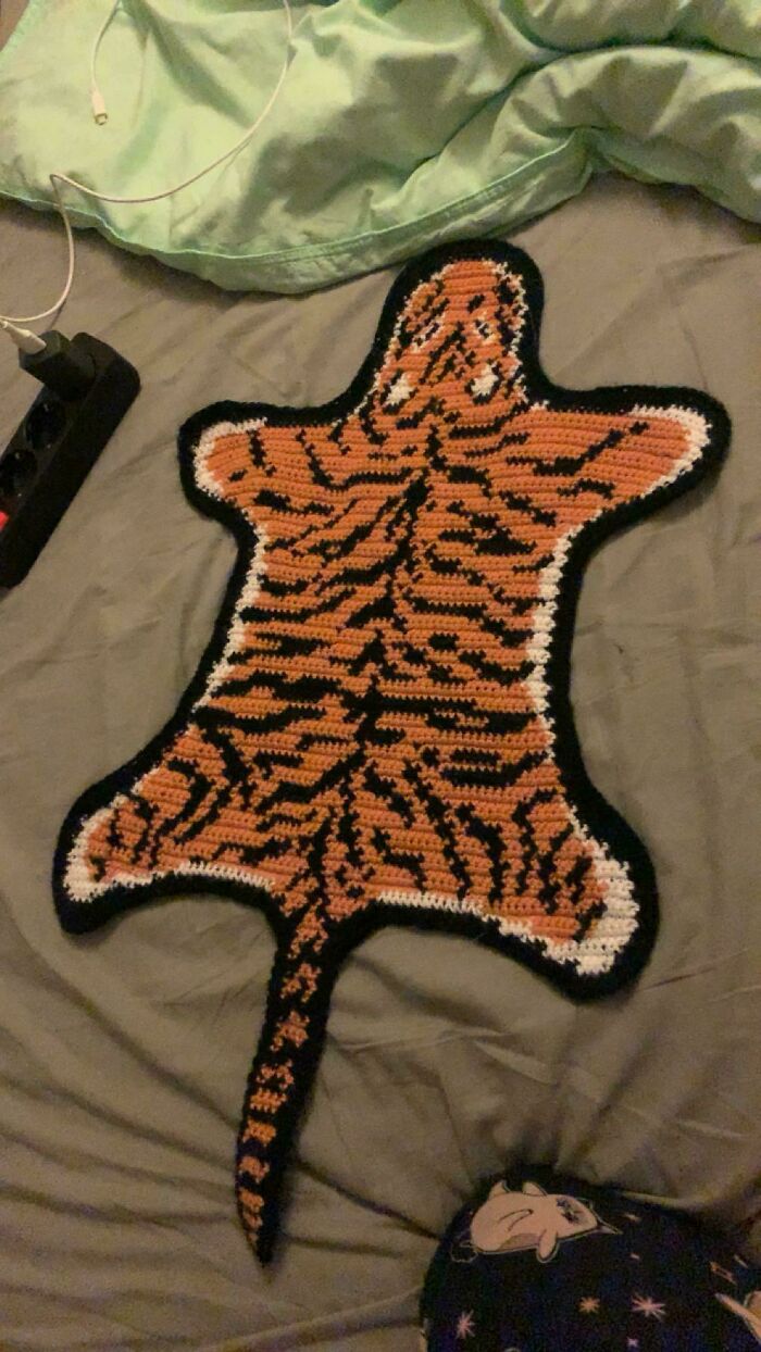Crochet masterpiece in the shape of a tiger rug with detailed orange, black, and white stitching on a bed.