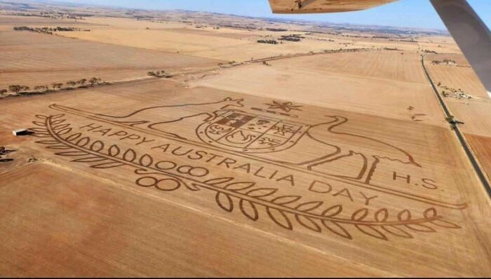 Aerial view of a field with a large "Happy Australia Day" design carved into the ground, showcasing Australian creativity.