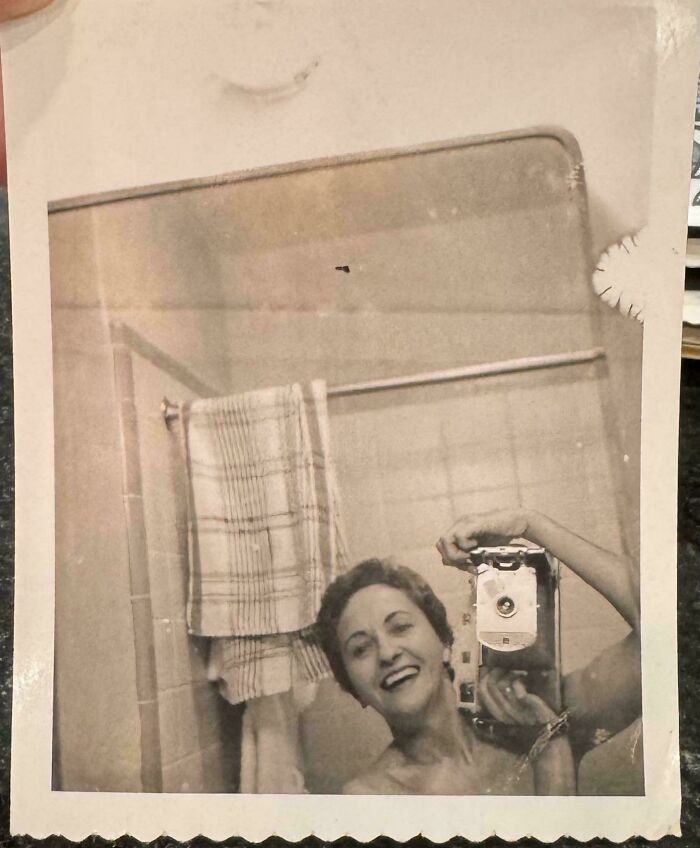 Vintage selfie of a smiling woman taking a photo in a bathroom mirror, showcasing fascinating old images from history.