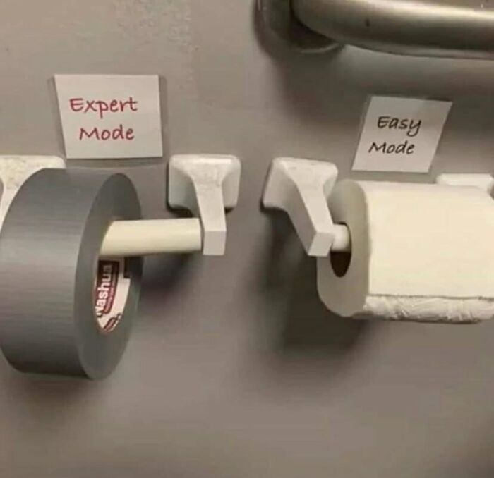 Two toilet paper holders labeled expert mode with duct tape roll and easy mode with regular toilet paper roll on a wall.