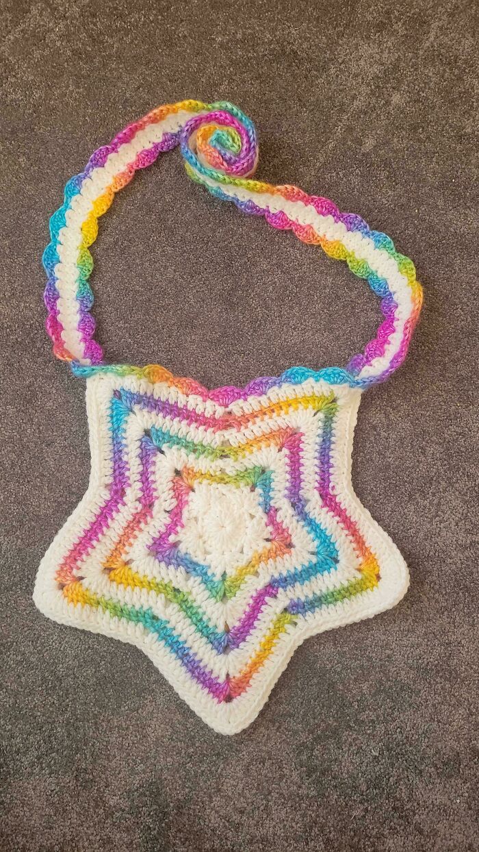 Colorful crocheted star-shaped bag with a rainbow strap, showcasing creative crochet masterpiece design on a neutral background