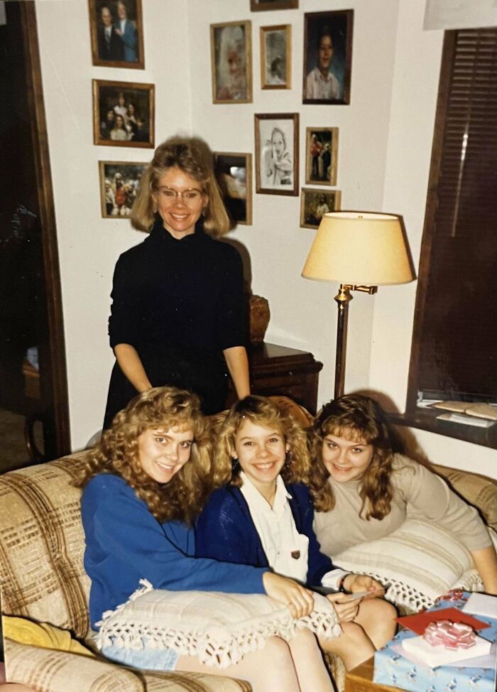 Women in an old photograph smiling on a couch in a living room, surrounded by picture frames on the wall.