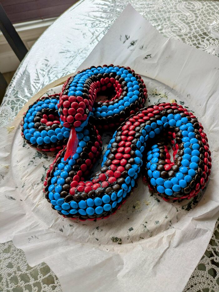Colorful snake-shaped cake with red and blue candies, showcasing a baker's culinary creativity.