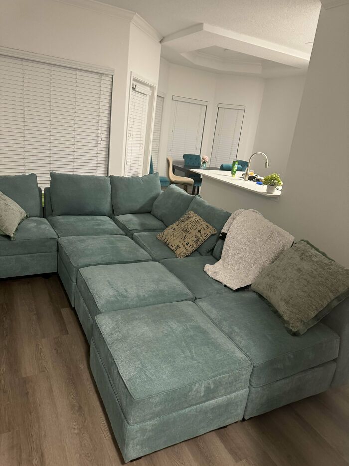 A large thrifted teal sectional sofa with cushions and blankets in a modern living room.