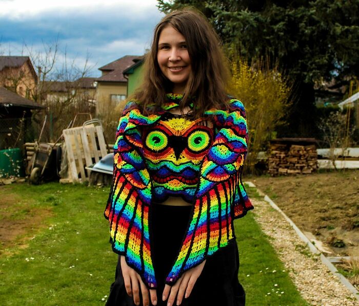 Young woman outdoors wearing a colorful rainbow crochet masterpiece with an owl design, showcasing vibrant crochet art.