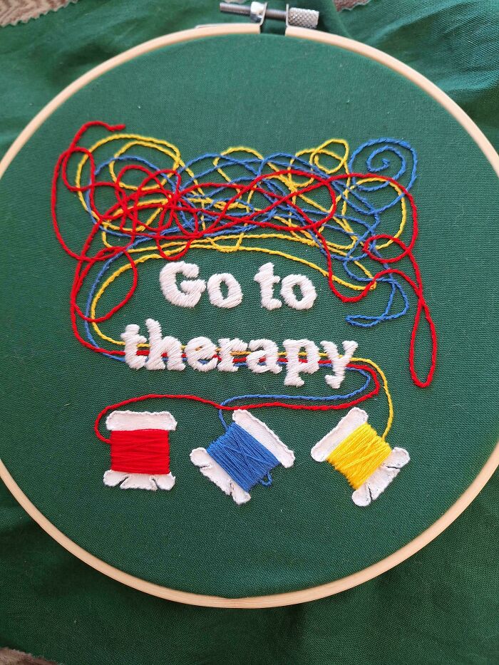 Embroidery hoop with colorful thread spools and stitched words "Go to therapy" on green fabric, showcasing embroidery skills.