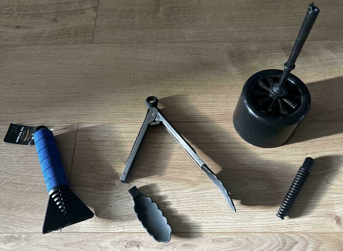 Low-quality items on wooden floor, including a blue-handled scraper, tongs, and a brush with holder.