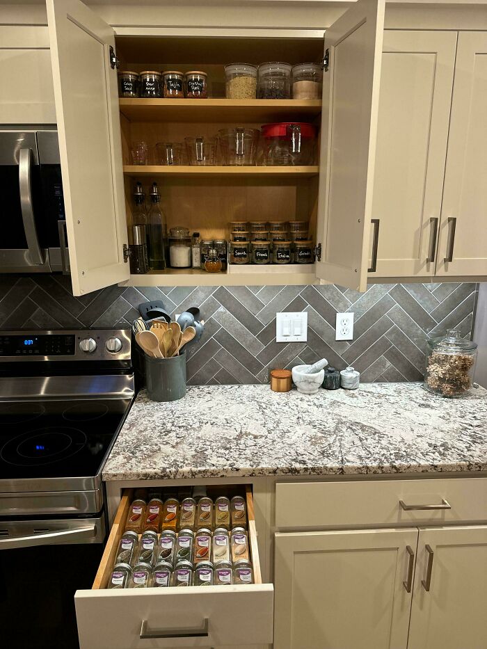 Organized kitchen with neatly arranged spices and jars in a drawer and cupboard, showcasing next-level organization.