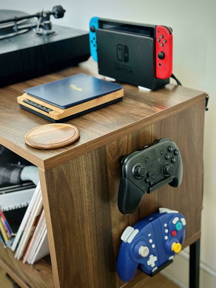 Neat organization of gaming setup with controllers mounted on a wooden shelf, featuring a Nintendo Switch and laptop.